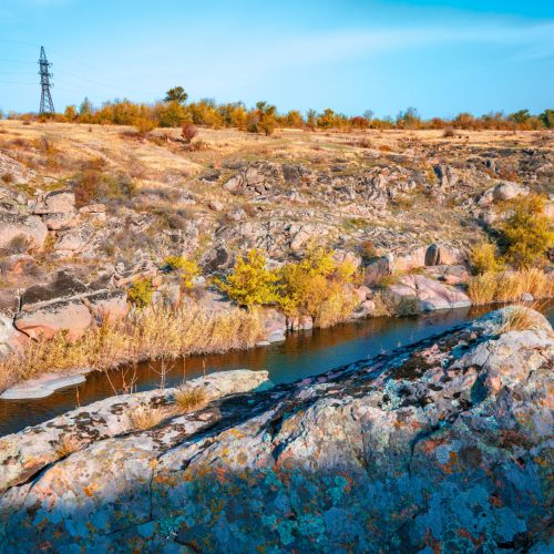 A large number of stone minerals covered with green vegetation lying above a small river in picturesque Ukraine and its beautiful nature